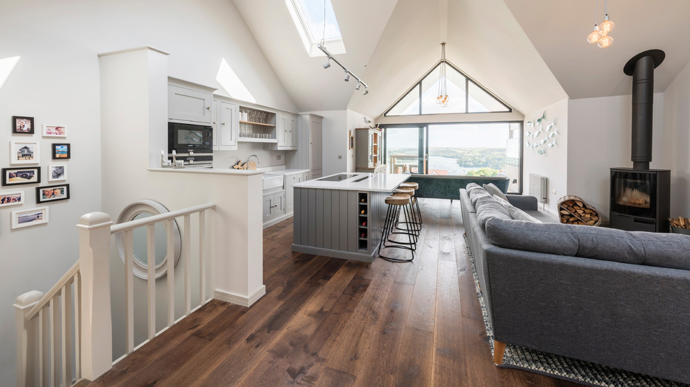 Large modern l-shaped open plan kitchen in Devon with a farmhouse sink, shaker cabinets, grey cabinets, solid surface benchtops, light hardwood floors and with island.