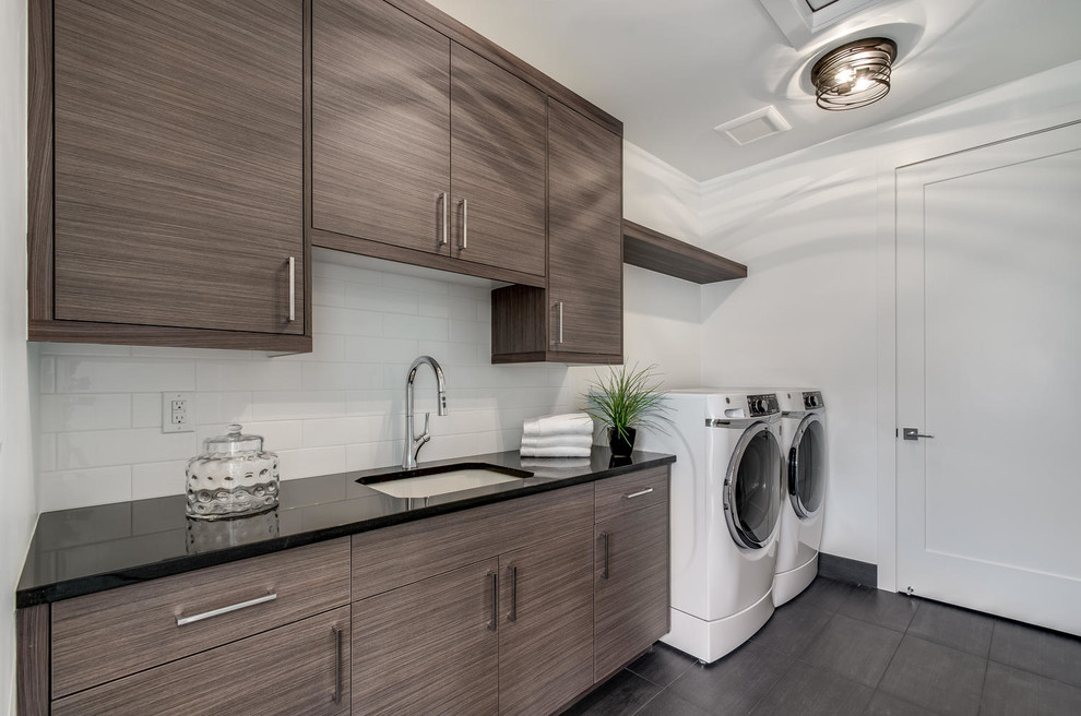 Design ideas for a mid-sized contemporary single-wall dedicated laundry room in Denver with an undermount sink, flat-panel cabinets, granite benchtops, white walls, porcelain floors, a side-by-side washer and dryer, grey floor and black benchtop.