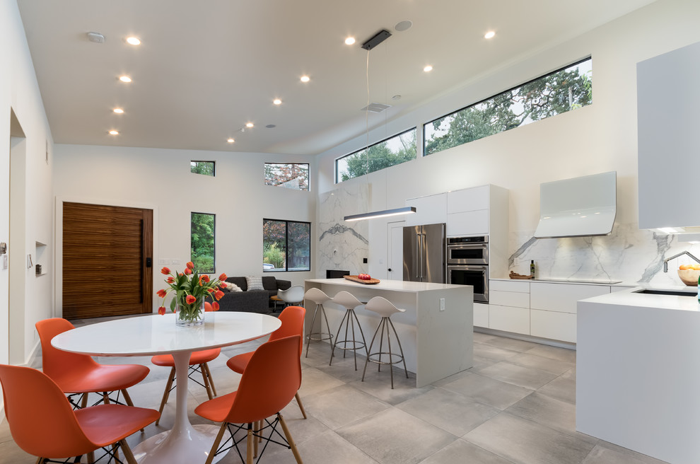 Inspiration for a mid-sized modern l-shaped open plan kitchen in Los Angeles with flat-panel cabinets, white cabinets, white splashback, stainless steel appliances, with island, quartzite benchtops, stone slab splashback, an undermount sink, concrete floors and grey floor.