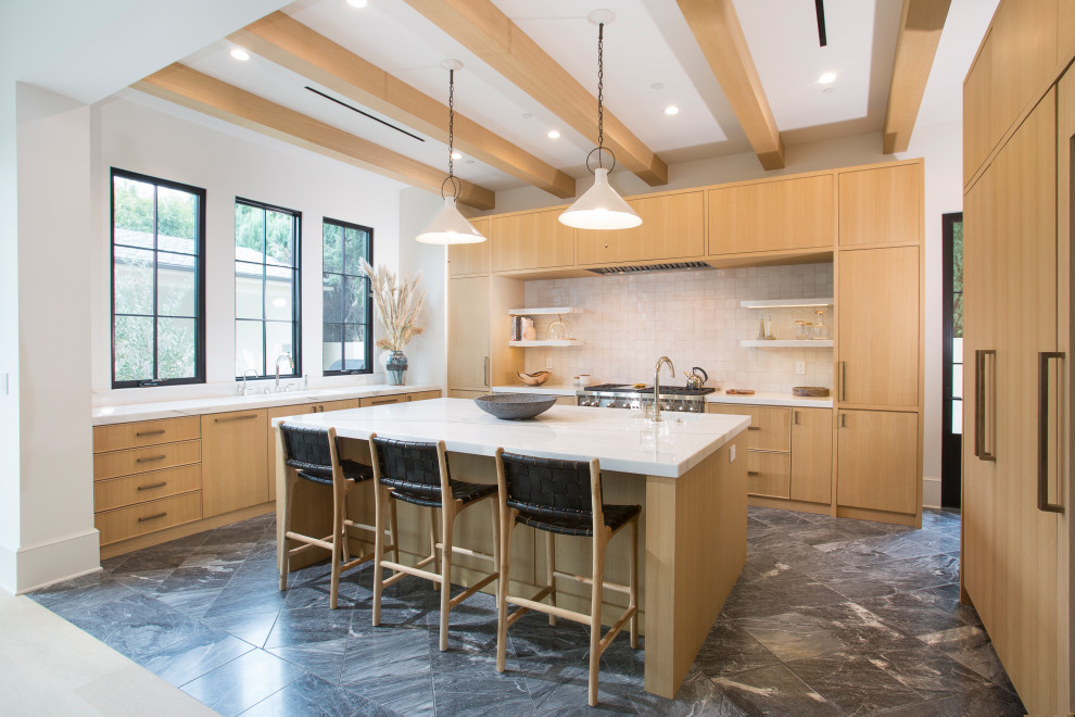 This is an example of a contemporary u-shaped kitchen in Los Angeles with flat-panel cabinets, medium wood cabinets, beige splashback, panelled appliances, with island, black floor and white benchtop.