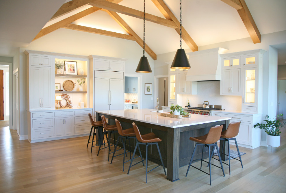 Design ideas for a large country l-shaped eat-in kitchen in Milwaukee with a farmhouse sink, shaker cabinets, white cabinets, quartz benchtops, white splashback, engineered quartz splashback, panelled appliances, light hardwood floors, with island, brown floor, white benchtop and vaulted.