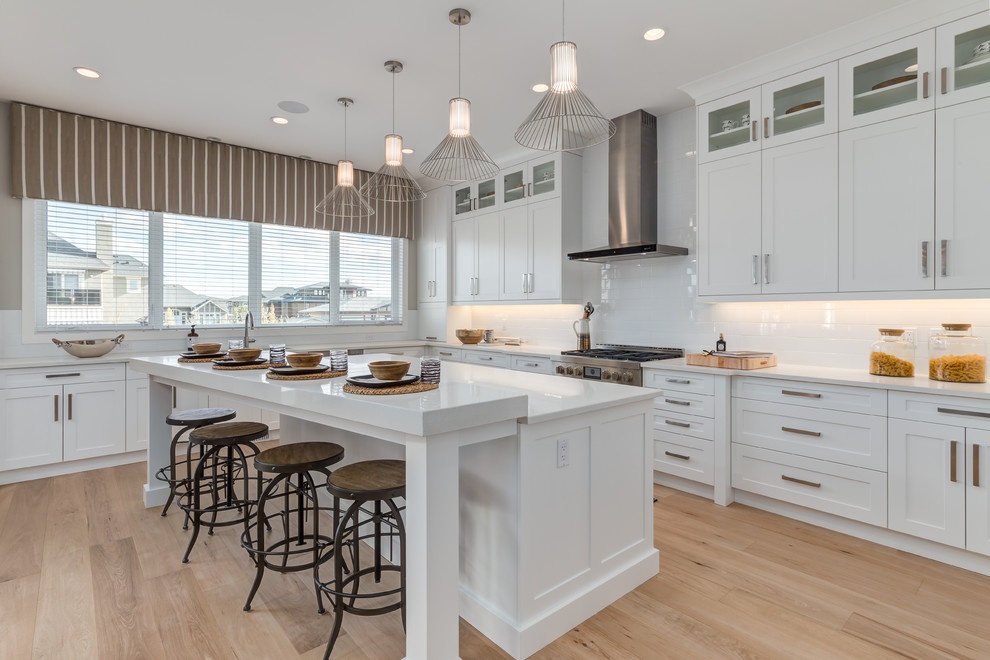 Photo of a large contemporary galley eat-in kitchen in Calgary with white cabinets, quartz benchtops, stainless steel appliances, a double-bowl sink, recessed-panel cabinets, white splashback, subway tile splashback, light hardwood floors and with island.