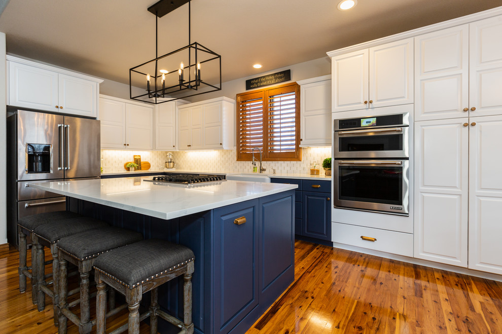 Mid-sized traditional l-shaped eat-in kitchen in Denver with a farmhouse sink, raised-panel cabinets, blue cabinets, wood benchtops, white splashback, marble splashback, stainless steel appliances, light hardwood floors, multiple islands and white benchtop.