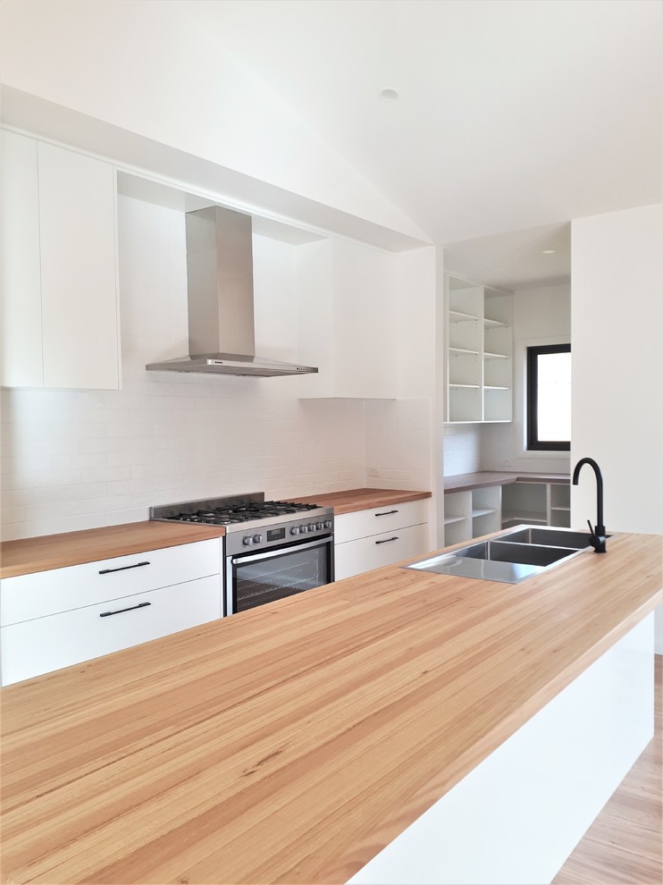 Design ideas for a contemporary galley kitchen in Other with a drop-in sink, flat-panel cabinets, white cabinets, wood benchtops, white splashback, subway tile splashback, stainless steel appliances, light hardwood floors, with island, brown floor and brown benchtop.