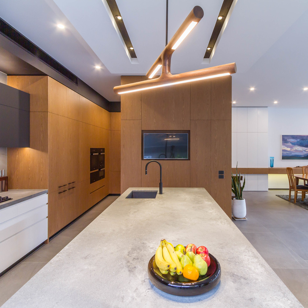 This is an example of a large modern galley open plan kitchen in Melbourne with an undermount sink, flat-panel cabinets, medium wood cabinets, quartz benchtops, grey splashback, porcelain splashback, black appliances, porcelain floors, with island, grey floor and grey benchtop.