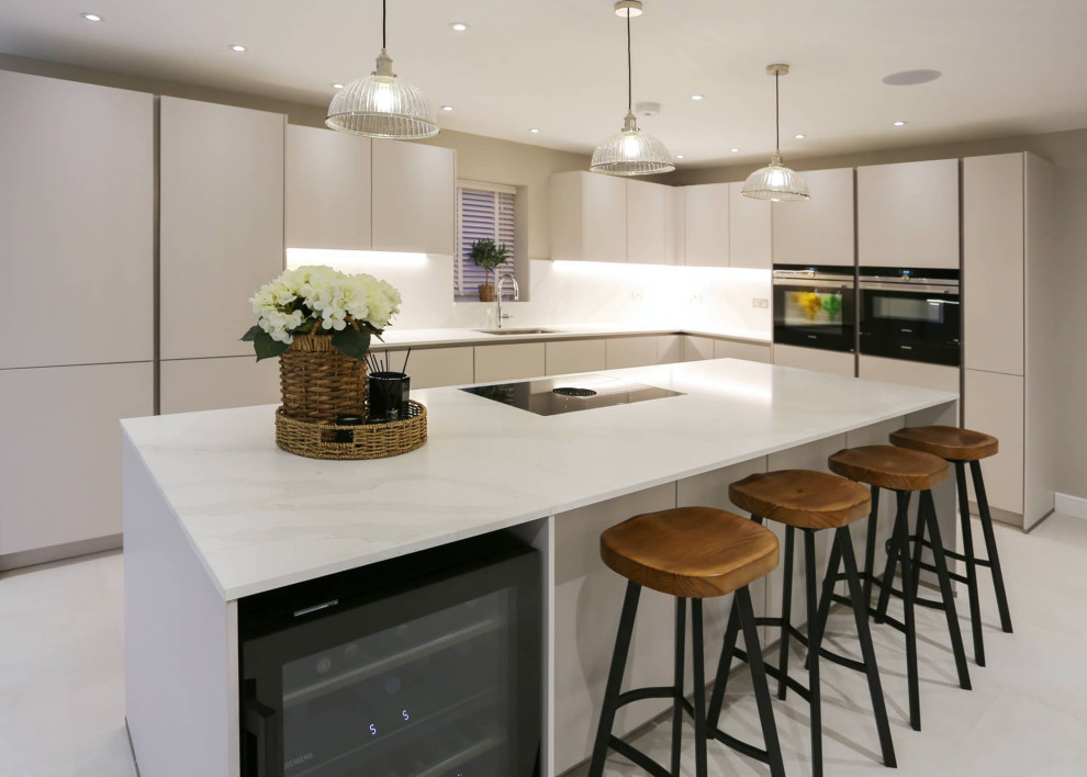 This is an example of a large scandinavian single-wall open plan kitchen in Hertfordshire with a single-bowl sink, flat-panel cabinets, white cabinets, quartz worktops, white splashback, black appliances, an island, white floors, white worktops and feature lighting.