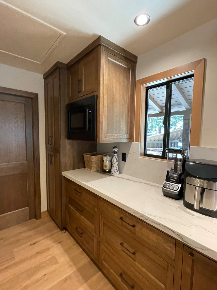 Example of a mid-sized transitional l-shaped light wood floor, beige floor and vaulted ceiling open concept kitchen design in Other with shaker cabinets, medium tone wood cabinets, quartz countertops, white backsplash, quartz backsplash, black appliances, an island and white countertops