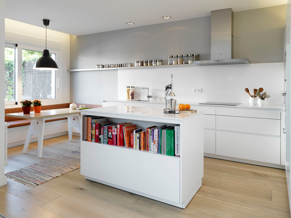 Design ideas for a mid-sized contemporary single-wall eat-in kitchen in Madrid with flat-panel cabinets, white cabinets, white splashback, with island, light hardwood floors and stainless steel appliances.