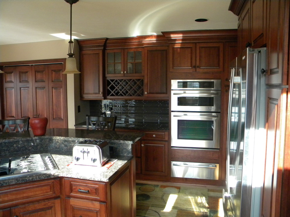 Example of a mid-sized transitional u-shaped light wood floor eat-in kitchen design with an undermount sink, raised-panel cabinets, medium tone wood cabinets, granite countertops, multicolored backsplash, stone tile backsplash, stainless steel appliances and an island
