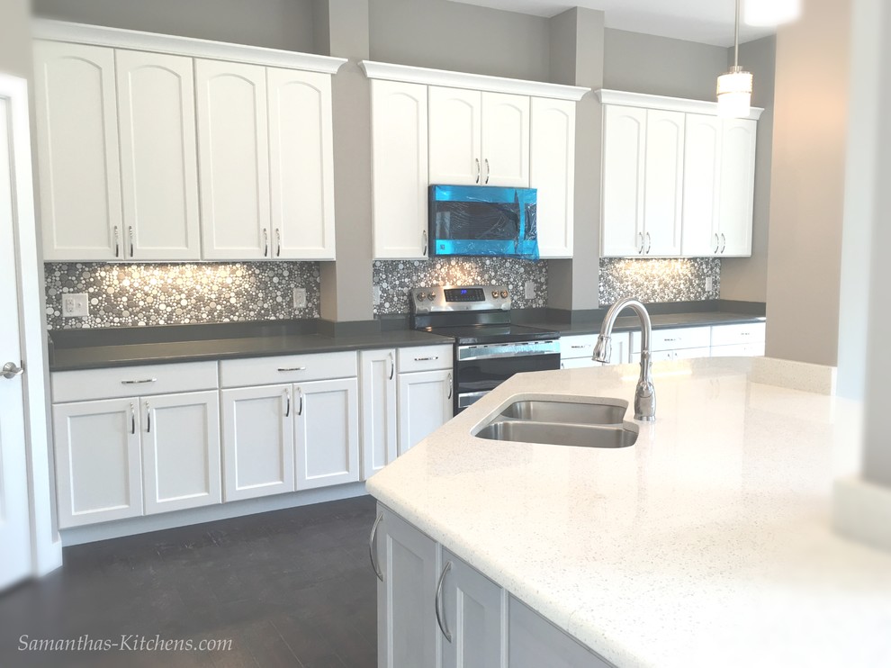 Mid-sized transitional l-shaped dark wood floor home design photo with an undermount sink, recessed-panel cabinets, gray cabinets, quartz countertops, white backsplash, ceramic backsplash, stainless steel appliances and an island
