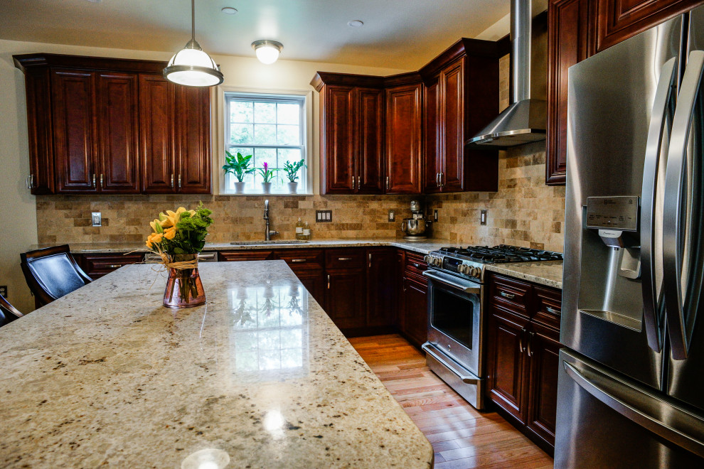 This is an example of a l-shaped eat-in kitchen in Philadelphia with an undermount sink, raised-panel cabinets, red cabinets, granite benchtops, beige splashback, stone tile splashback, light hardwood floors, with island, yellow floor and beige benchtop.