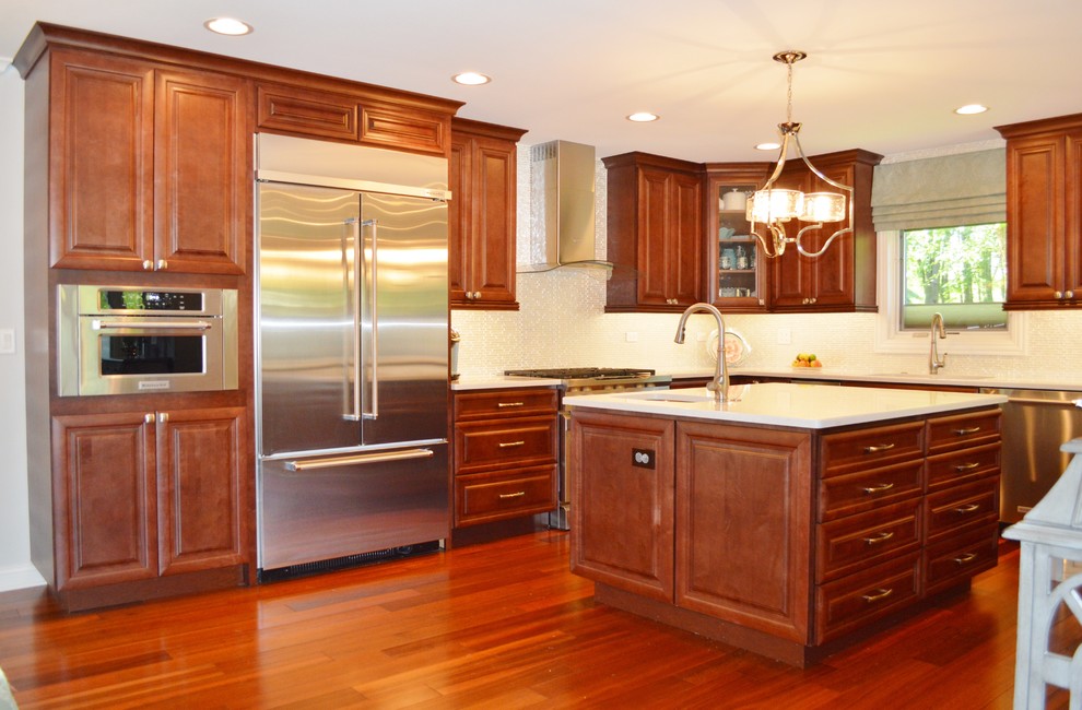 Example of a large transitional l-shaped open concept kitchen design in Chicago with an undermount sink, raised-panel cabinets, medium tone wood cabinets, quartz countertops, white backsplash, glass tile backsplash, stainless steel appliances and an island