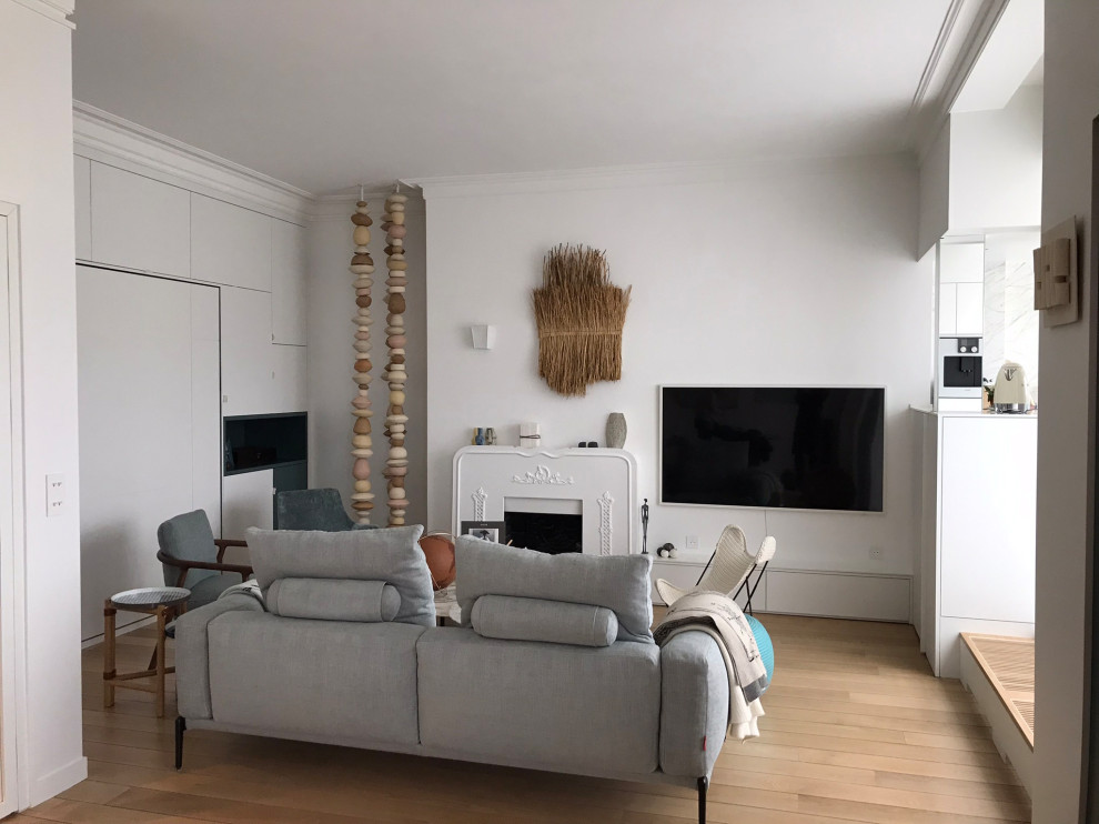 This is an example of a contemporary living room in Paris with white walls, light hardwood floors, a standard fireplace, a metal fireplace surround and a wall-mounted tv.