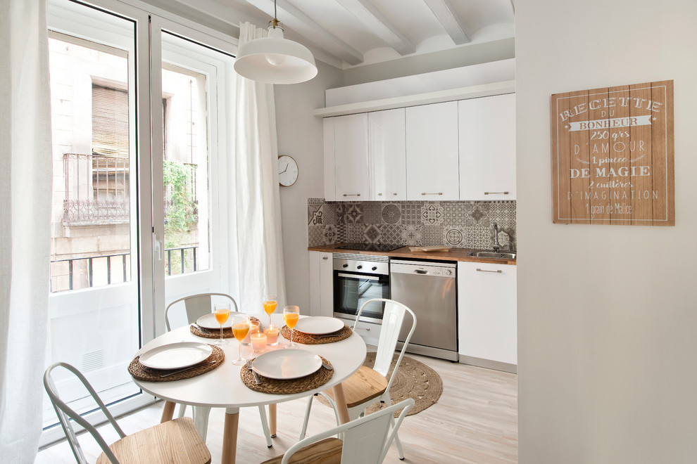 This is an example of a small transitional single-wall eat-in kitchen in Barcelona with flat-panel cabinets, white cabinets, wood benchtops, multi-coloured splashback, ceramic splashback, stainless steel appliances, light hardwood floors, no island, beige floor and a drop-in sink.