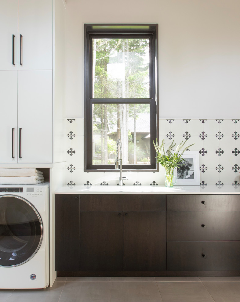Medium sized modern single-wall separated utility room in Seattle with flat-panel cabinets, black cabinets, composite countertops, white splashback, cement tile splashback, white walls, porcelain flooring, a side by side washer and dryer, grey floors, white worktops and exposed beams.