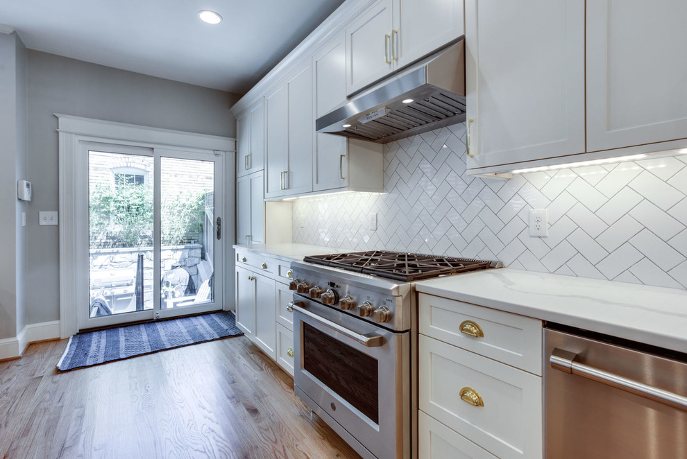 Example of a mid-sized transitional galley light wood floor and beige floor eat-in kitchen design in DC Metro with a farmhouse sink, shaker cabinets, white cabinets, quartz countertops, white backsplash, subway tile backsplash, stainless steel appliances, a peninsula and white countertops