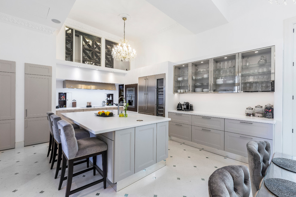 This is an example of a large traditional l-shaped open plan kitchen in Other with recessed-panel cabinets, grey cabinets, white splashback, stainless steel appliances, with island and white benchtop.
