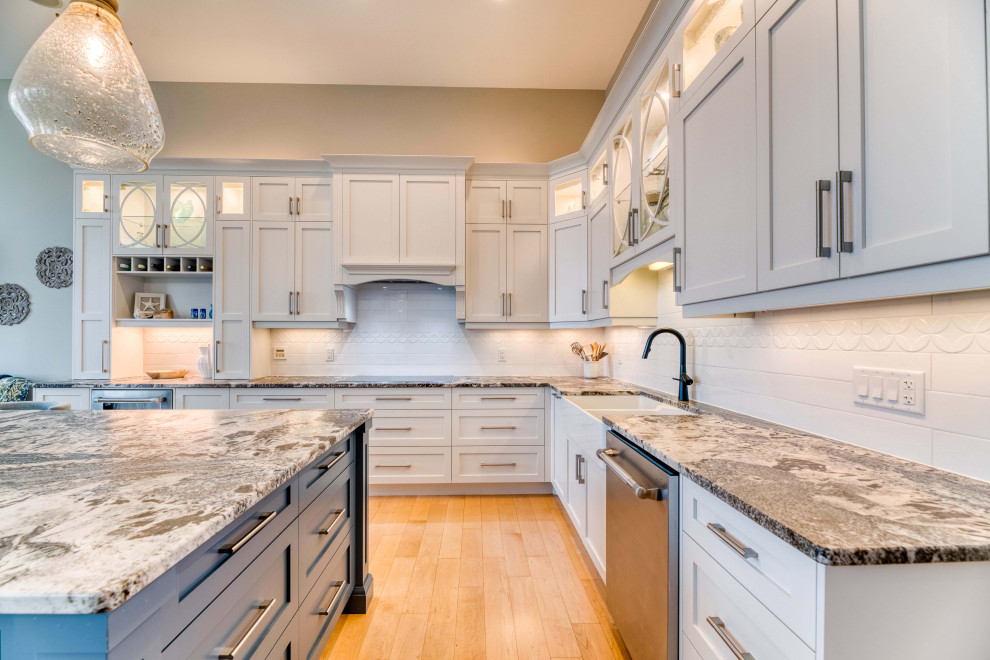 Example of a large transitional l-shaped light wood floor and brown floor eat-in kitchen design with a farmhouse sink, shaker cabinets, white cabinets, granite countertops, ceramic backsplash, stainless steel appliances and an island