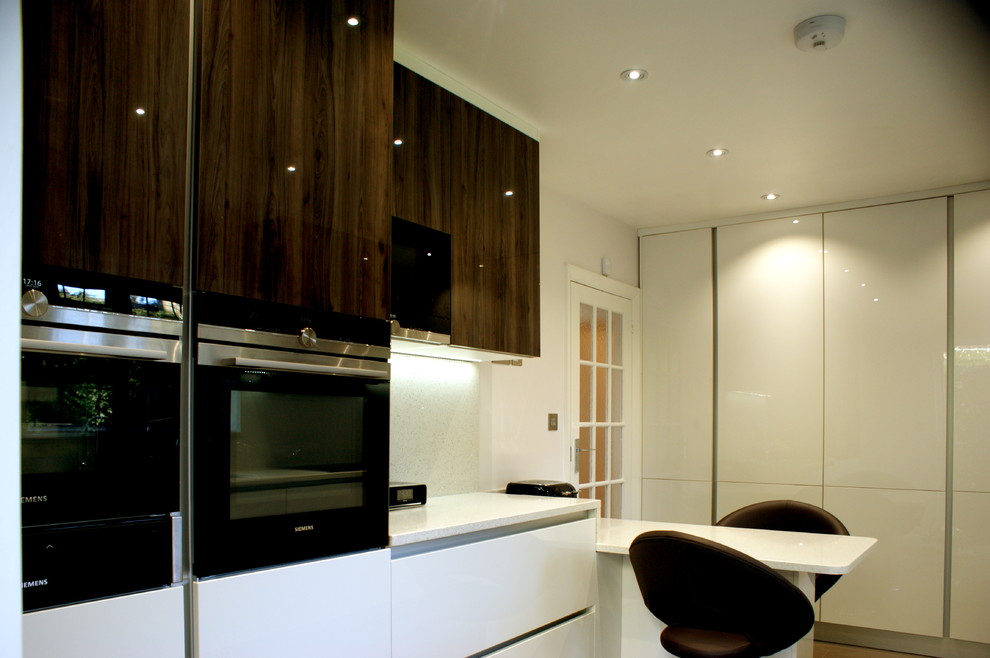 Design ideas for a large modern galley enclosed kitchen in London with a built-in sink, flat-panel cabinets, white cabinets, quartz worktops, white splashback, stone slab splashback, black appliances and porcelain flooring.