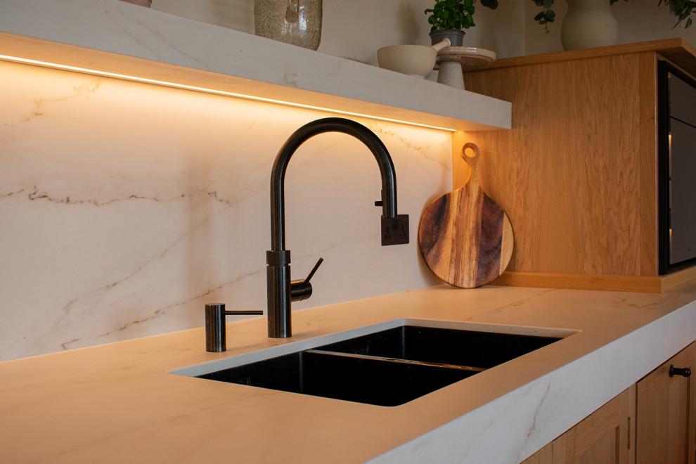 Large contemporary open plan kitchen in Kent with medium wood cabinets, engineered stone countertops, white splashback, light hardwood flooring, an island, white worktops, a wood ceiling and feature lighting.