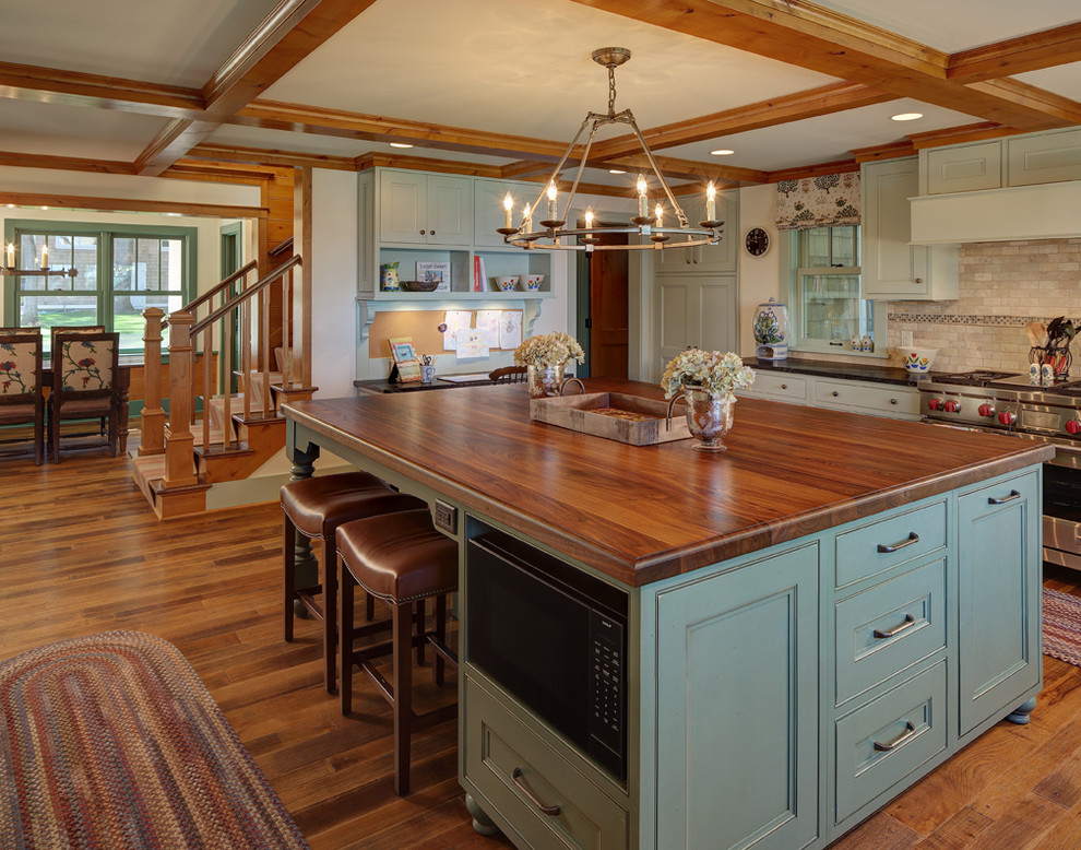 This is an example of a country u-shaped kitchen in Milwaukee with a farmhouse sink, beaded inset cabinets, green cabinets, beige splashback, stone tile splashback, panelled appliances, medium hardwood floors, with island and wood benchtops.