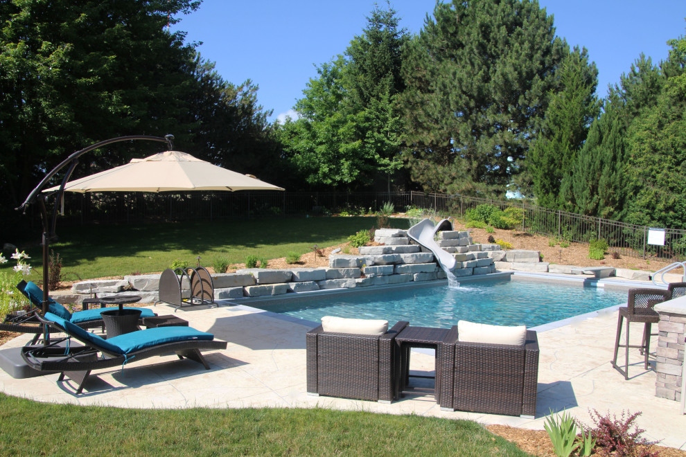 Пример оригинального дизайна: большой естественный, прямоугольный бассейн на заднем дворе в стиле рустика с водной горкой и настилом