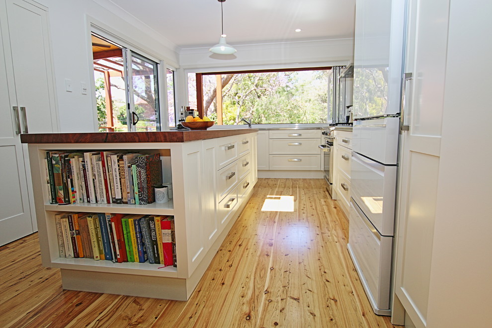 Inspiration for a mid-sized transitional l-shaped kitchen pantry in Sydney with a double-bowl sink, shaker cabinets, white cabinets, wood benchtops, black splashback, glass sheet splashback, stainless steel appliances, light hardwood floors and with island.