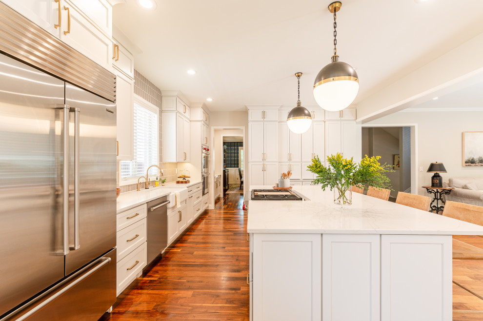 Inspiration for a large transitional l-shaped dark wood floor and brown floor open concept kitchen remodel in Denver with a farmhouse sink, shaker cabinets, beige cabinets, quartz countertops, beige backsplash, ceramic backsplash, stainless steel appliances, an island and white countertops
