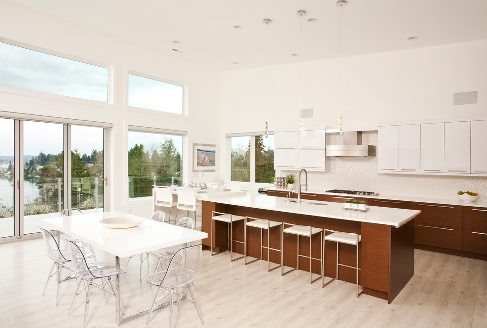This is an example of a contemporary galley eat-in kitchen in Seattle with flat-panel cabinets, white splashback, white cabinets, light hardwood floors, with island and stainless steel appliances.