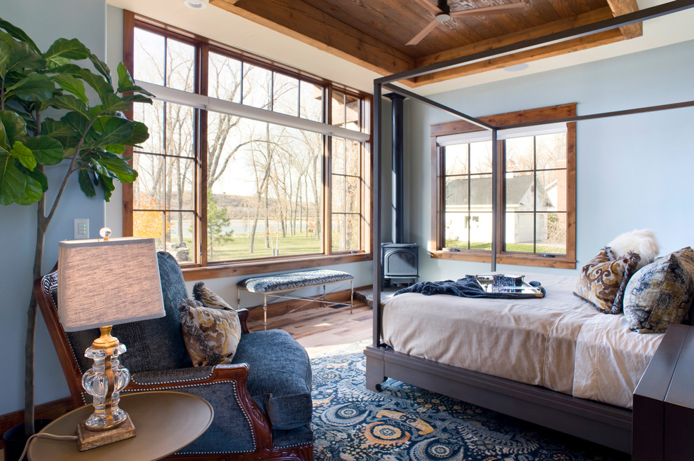 Mid-sized transitional master bedroom in Other with blue walls, light hardwood floors, a wood stove and brown floor.