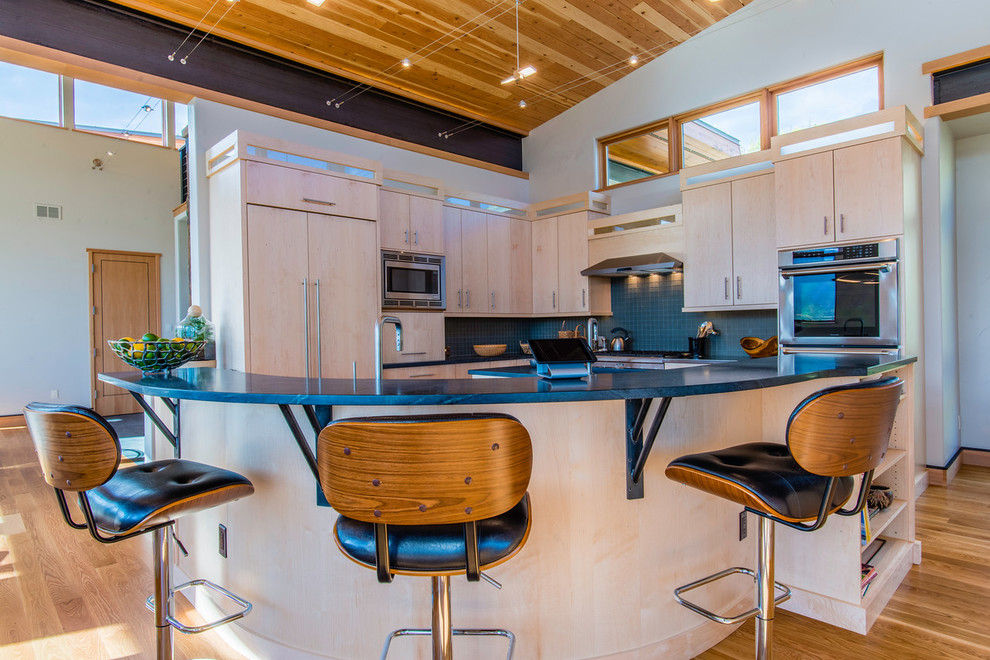 Photo of a mid-sized modern u-shaped eat-in kitchen in Denver with flat-panel cabinets, light wood cabinets, limestone benchtops, blue splashback, glass tile splashback, stainless steel appliances, light hardwood floors, with island and brown floor.