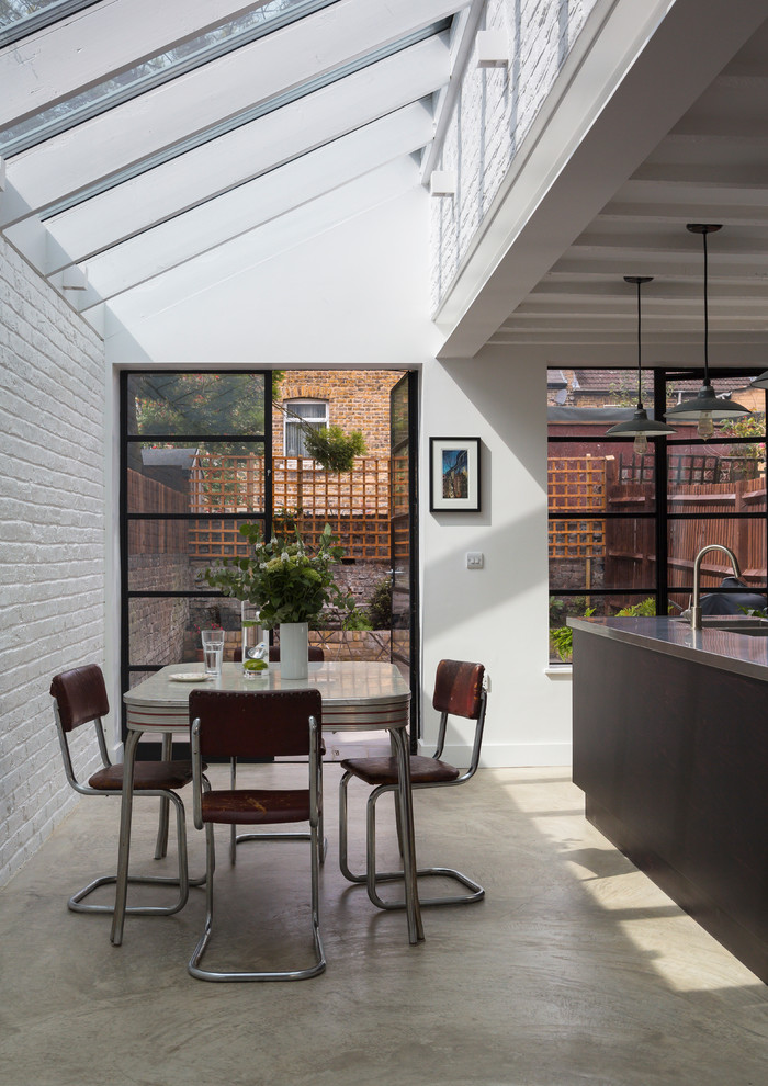 This is an example of a contemporary kitchen/dining combo in London with white walls and concrete floors.