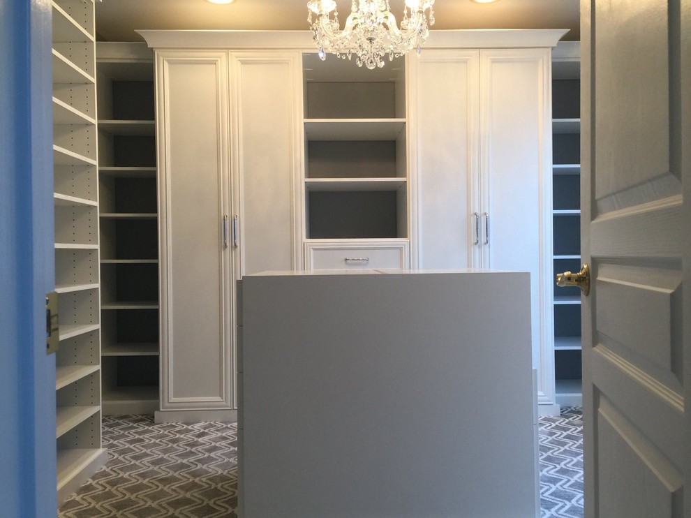This is an example of a large traditional women's walk-in wardrobe in New York with recessed-panel cabinets, carpet and beige floor.