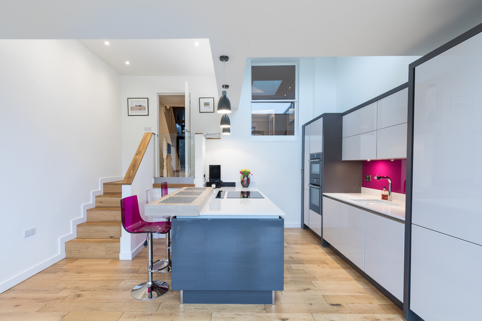 This is an example of a large contemporary galley eat-in kitchen in Hampshire with an integrated sink, flat-panel cabinets, grey cabinets, quartzite benchtops, pink splashback, glass tile splashback, panelled appliances, medium hardwood floors and with island.