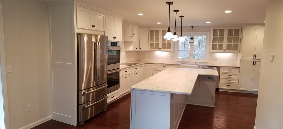 This is an example of a mid-sized transitional l-shaped eat-in kitchen in Other with a farmhouse sink, shaker cabinets, white cabinets, granite benchtops, white splashback, subway tile splashback, stainless steel appliances, dark hardwood floors, with island and brown floor.