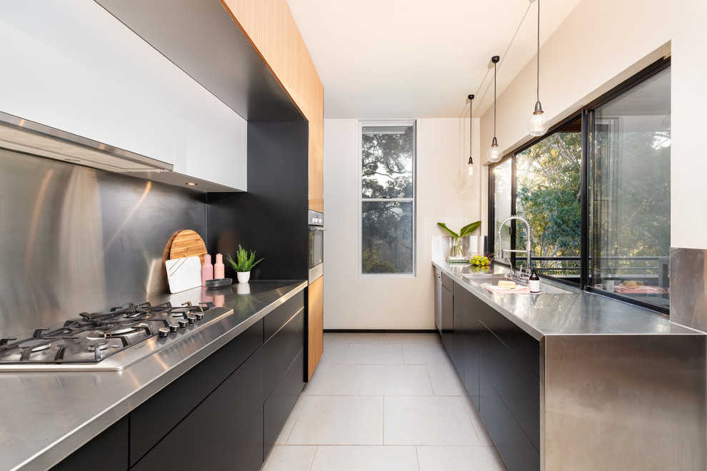 This is an example of a contemporary kitchen in Other with an integrated sink, flat-panel cabinets, black cabinets, stainless steel benchtops, metallic splashback, no island, white floor and grey benchtop.