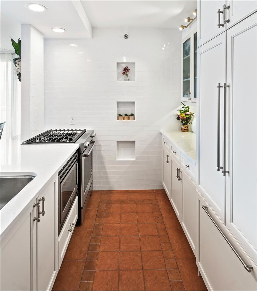 Design ideas for a small transitional galley separate kitchen in New York with an undermount sink, glass-front cabinets, beige cabinets, quartz benchtops, white splashback, stone tile splashback, panelled appliances and terra-cotta floors.