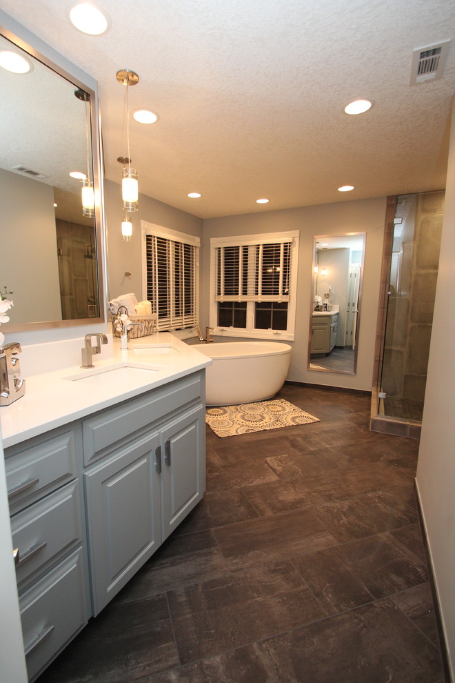 Large transitional master bathroom in Other with raised-panel cabinets, grey cabinets, a freestanding tub, a corner shower, a two-piece toilet, gray tile, porcelain tile, grey walls, porcelain floors, an undermount sink, engineered quartz benchtops, grey floor and a hinged shower door.