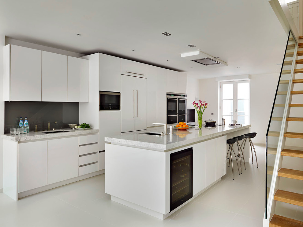 Large contemporary open plan kitchen in London with with island, flat-panel cabinets, white cabinets, quartz benchtops, stainless steel appliances and an undermount sink.