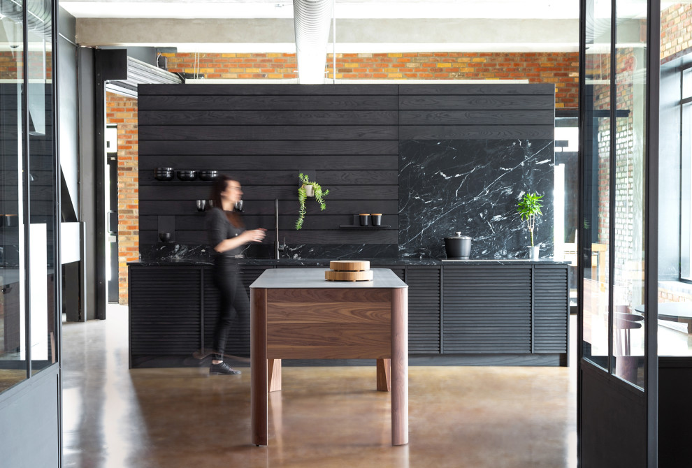 Idéer för mellanstora industriella linjära svart kök, med en undermonterad diskho, luckor med lamellpanel, svarta skåp, marmorbänkskiva, svart stänkskydd, stänkskydd i trä, integrerade vitvaror, betonggolv, en köksö och beiget golv
