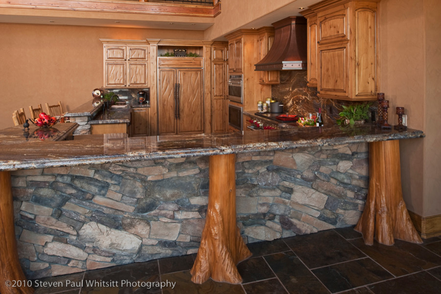 Open concept kitchen - huge rustic u-shaped slate floor open concept kitchen idea with an undermount sink, raised-panel cabinets, distressed cabinets, granite countertops, multicolored backsplash, stone slab backsplash, stainless steel appliances and a peninsula