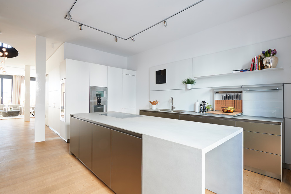 Design ideas for a mid-sized contemporary l-shaped eat-in kitchen in Hamburg with flat-panel cabinets, white splashback, glass sheet splashback, stainless steel appliances, medium hardwood floors, with island, brown floor, white benchtop, a double-bowl sink and white cabinets.