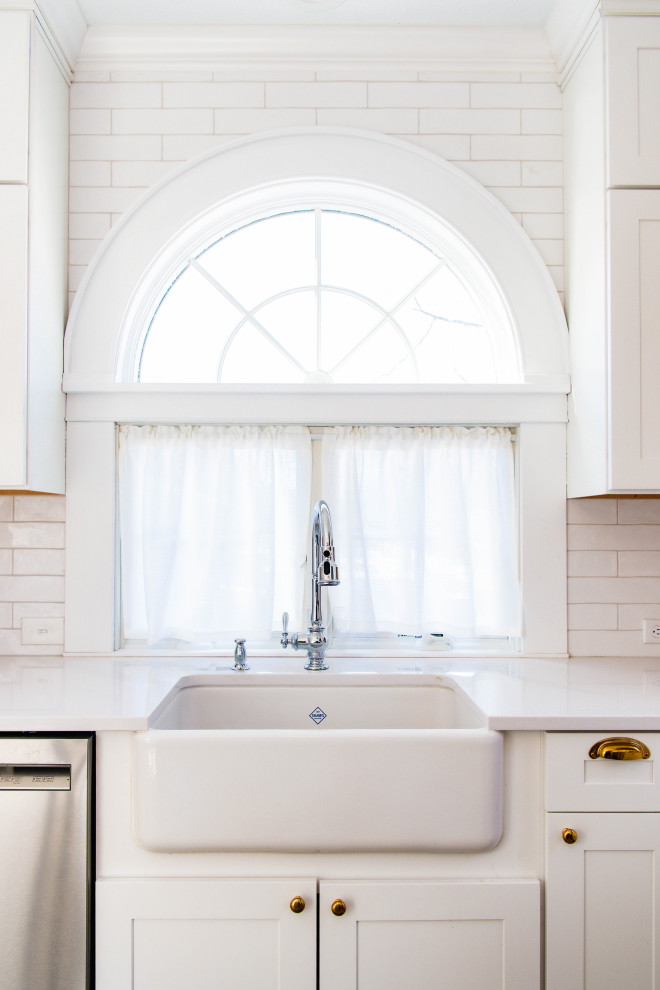 Bild på ett avskilt, stort vit vitt l-kök, med en rustik diskho, skåp i shakerstil, blå skåp, bänkskiva i kvarts, vitt stänkskydd, stänkskydd i tunnelbanekakel, rostfria vitvaror, ljust trägolv, en köksö och brunt golv