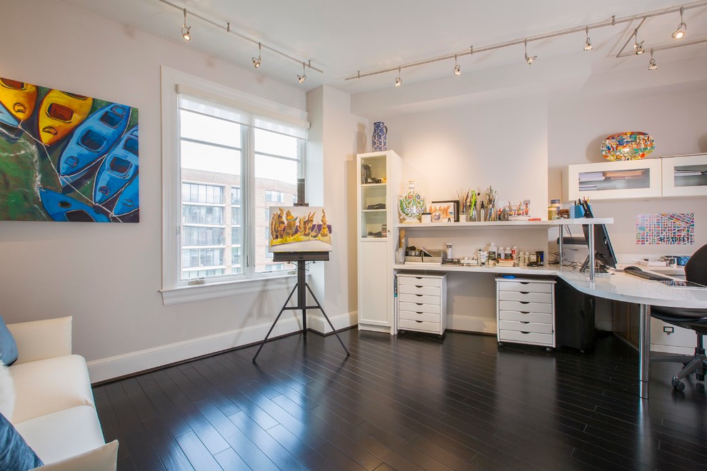 This is an example of a small contemporary home studio in DC Metro with white walls, dark hardwood floors and a built-in desk.
