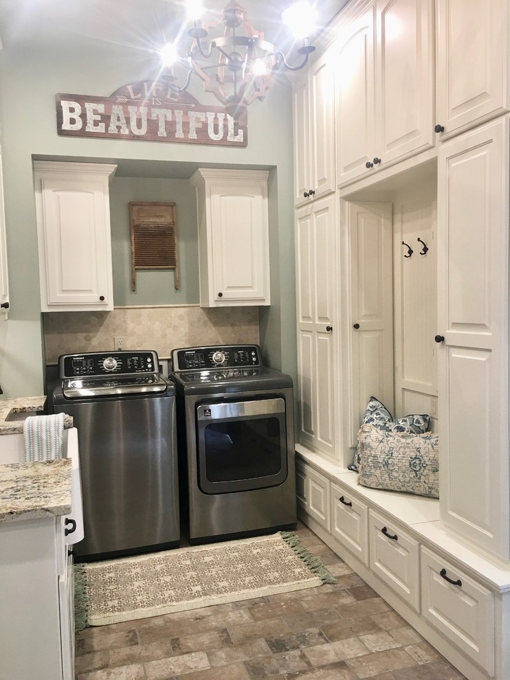 This is an example of a mid-sized transitional dedicated laundry room with a farmhouse sink, recessed-panel cabinets, white cabinets, granite benchtops, blue walls, brick floors, a side-by-side washer and dryer, beige floor and white benchtop.