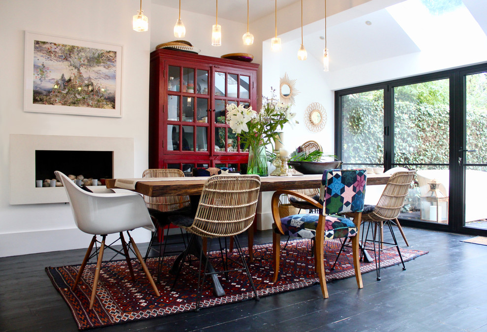 This is an example of an eclectic dining room in London with white walls, dark hardwood floors, a ribbon fireplace and black floor.
