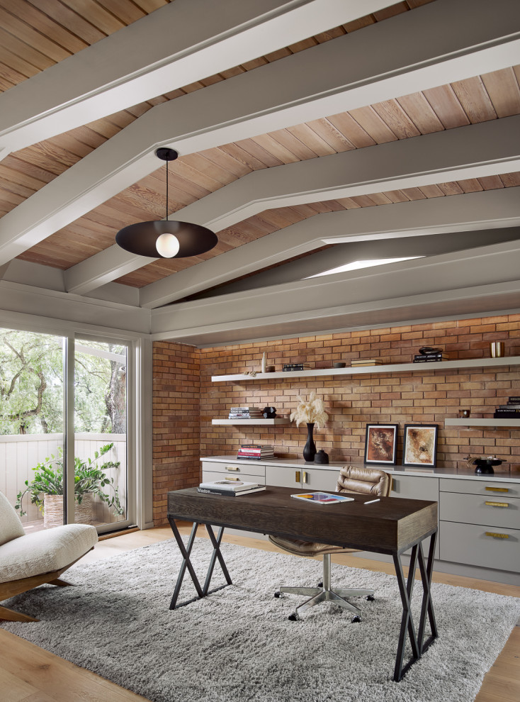 This is an example of a midcentury home office in Austin with light hardwood floors, a freestanding desk, beige floor, exposed beam, wood and brick walls.