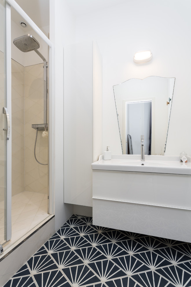Small contemporary 3/4 bathroom in Paris with white walls, an integrated sink, blue floor, a sliding shower screen, a curbless shower, white tile, flat-panel cabinets, white cabinets, a two-piece toilet, ceramic tile, cement tiles, solid surface benchtops and white benchtops.