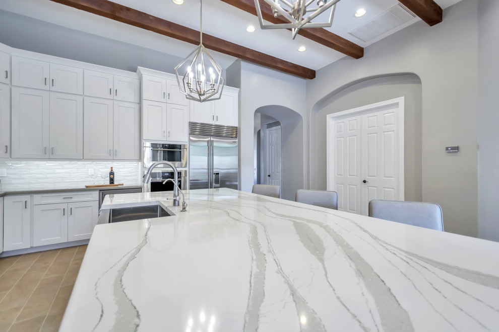 Eat-in kitchen - large transitional l-shaped porcelain tile and brown floor eat-in kitchen idea in Phoenix with a farmhouse sink, shaker cabinets, white cabinets, quartz countertops, white backsplash, subway tile backsplash, stainless steel appliances, an island and gray countertops