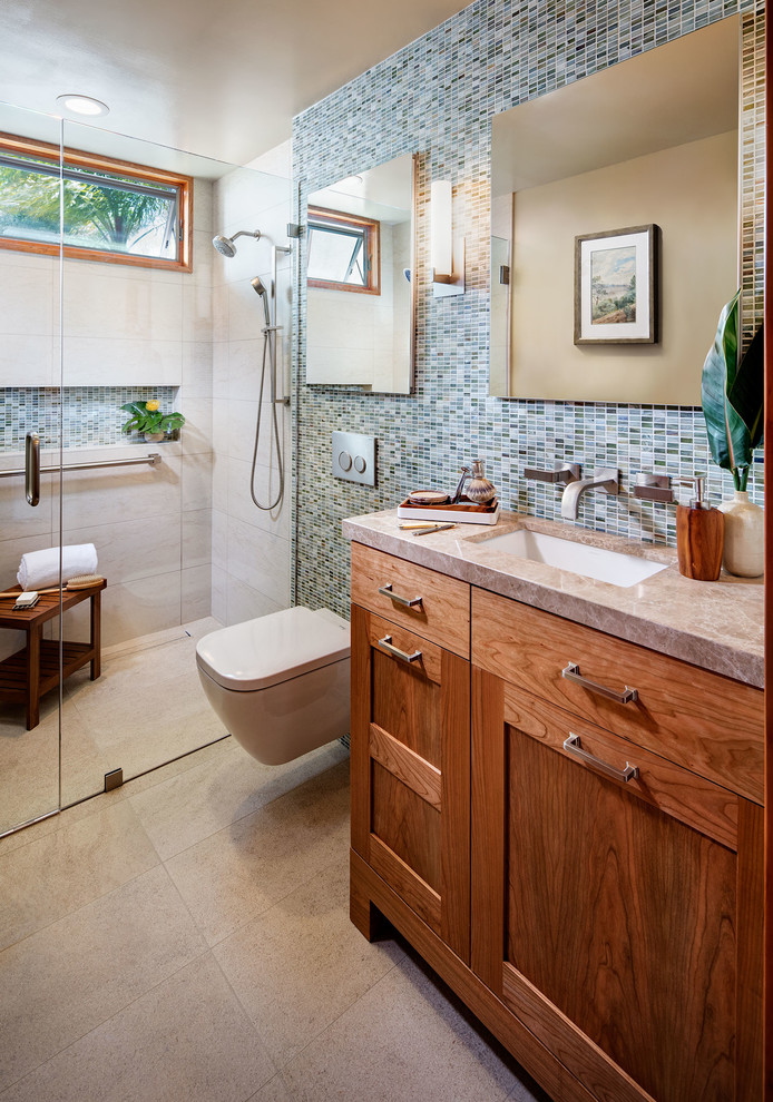 This is an example of a small contemporary 3/4 bathroom in San Diego with shaker cabinets, medium wood cabinets, a curbless shower, a wall-mount toilet, multi-coloured tile, glass sheet wall, beige walls, ceramic floors and an undermount sink.